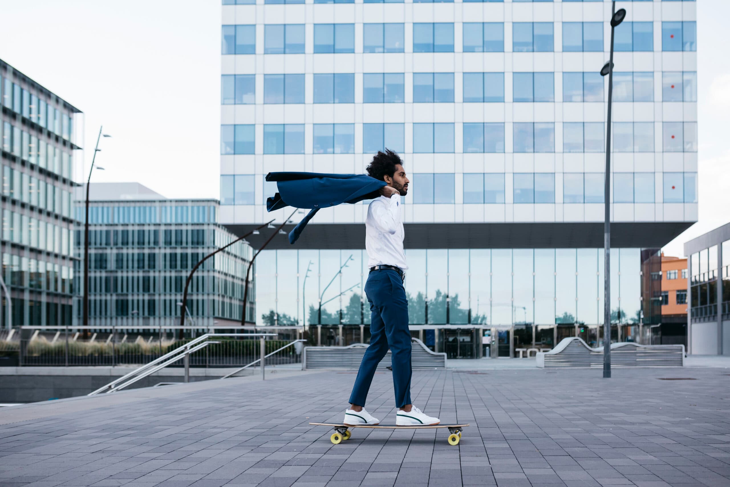 jeune homme faisant du skateboard devant un immeuble de bureau.